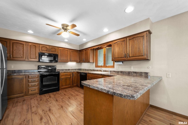 kitchen featuring brown cabinets, a sink, ceiling fan, black appliances, and a peninsula