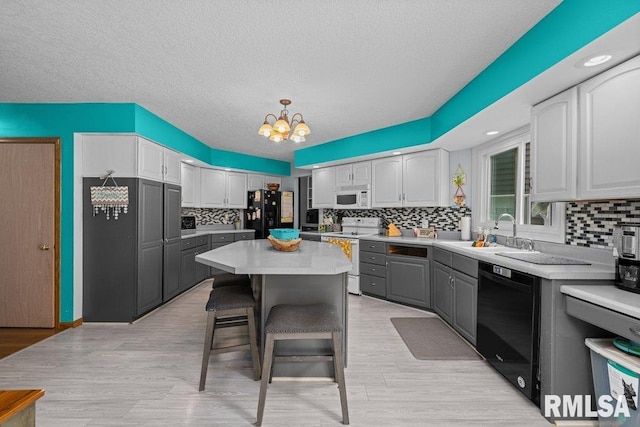 kitchen with black appliances, gray cabinets, tasteful backsplash, a sink, and a notable chandelier