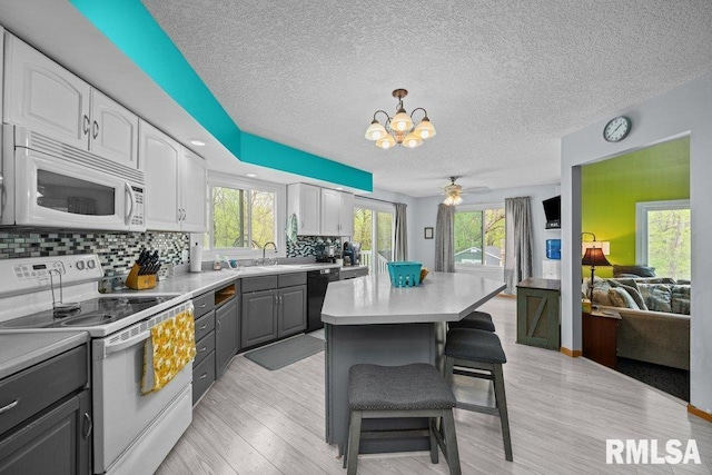 kitchen featuring decorative backsplash, gray cabinets, a kitchen breakfast bar, and white appliances