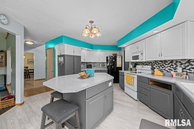 kitchen with a kitchen breakfast bar, gray cabinets, white appliances, and a notable chandelier