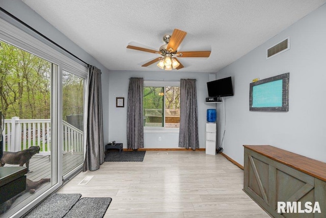 doorway featuring a ceiling fan, a textured ceiling, visible vents, light wood-type flooring, and baseboards