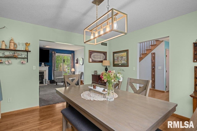 dining room featuring an inviting chandelier, visible vents, wood finished floors, a fireplace, and a textured ceiling