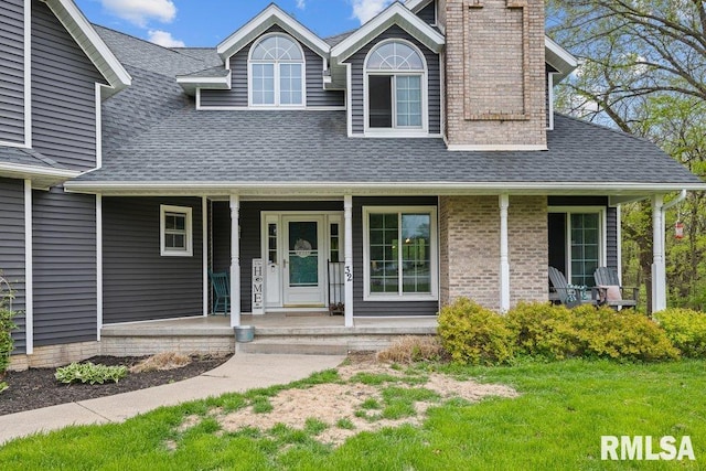 view of front of home with covered porch, a shingled roof, a chimney, and a front yard