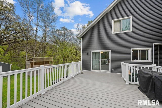 wooden terrace featuring a lawn, a grill, an outdoor structure, and a storage unit