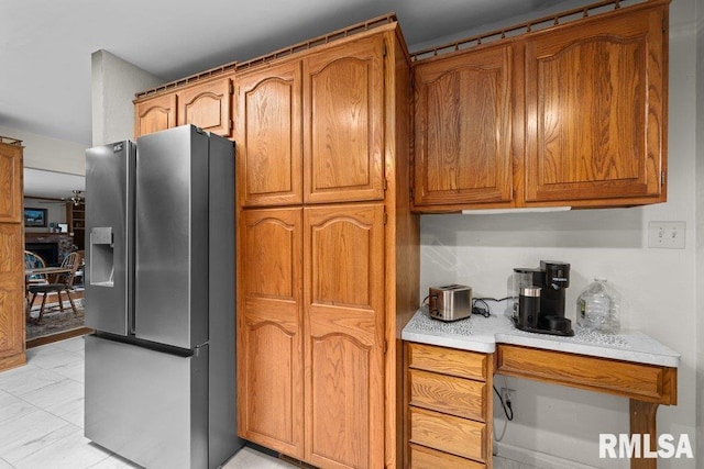 kitchen featuring stainless steel refrigerator with ice dispenser, brown cabinets, light countertops, and marble finish floor