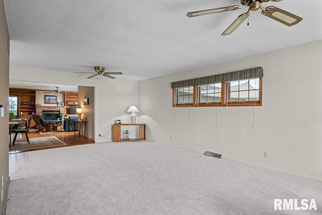 carpeted living area with baseboards, visible vents, ceiling fan, and a glass covered fireplace