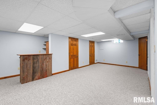 basement with baseboards, a bar, carpet, and a drop ceiling