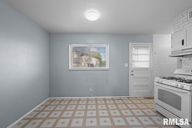 kitchen featuring light floors, white gas range oven, under cabinet range hood, and white cabinets