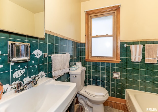 full bathroom featuring toilet, tile walls, a bathing tub, a wainscoted wall, and a sink