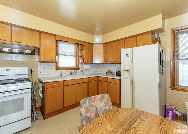 kitchen featuring a sink, light countertops, under cabinet range hood, and white appliances