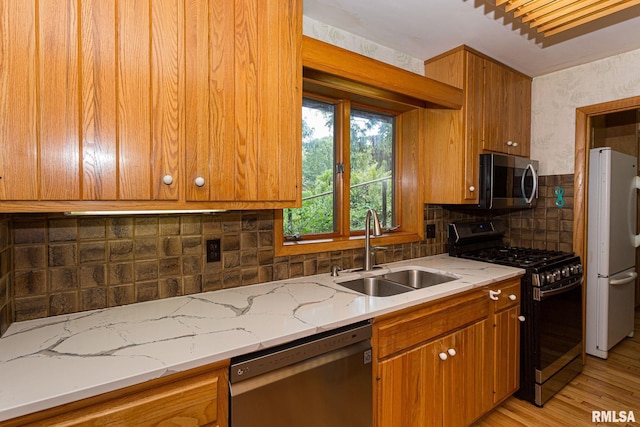 28018 230th St, Le Claire, IA 52753 - kitchen with appliances with stainless steel finishes, a sink, light wood-style floors, brown cabinetry, and tasteful backsplash