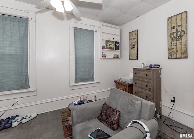 living area featuring ceiling fan, a drop ceiling, and wood finished floors