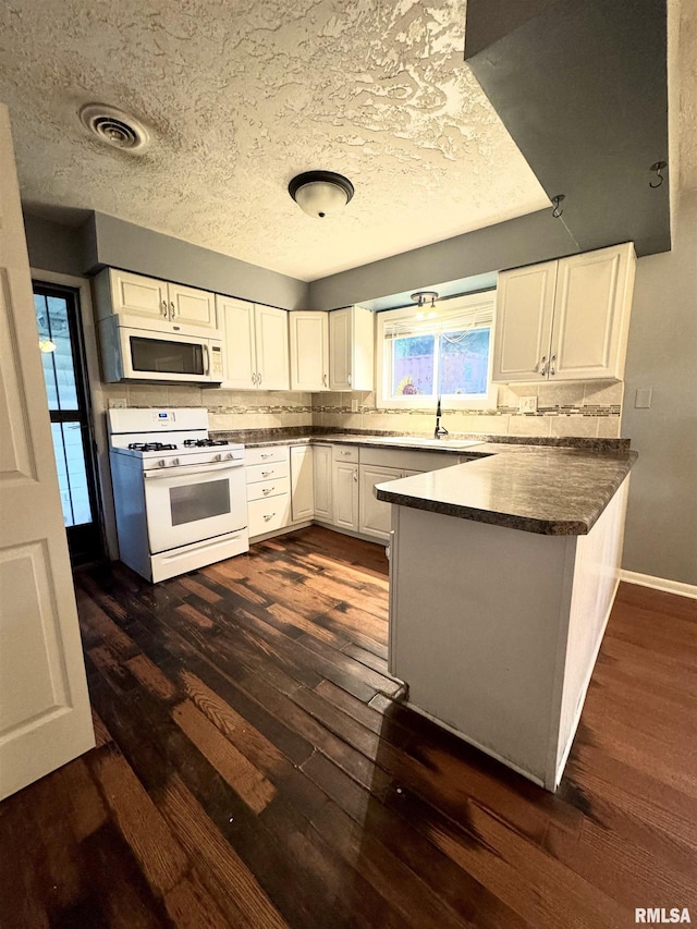 1001 W 6th St, West Frankfort, IL 62896 - kitchen featuring dark wood-style flooring, visible vents, a peninsula, white appliances, and white cabinetry