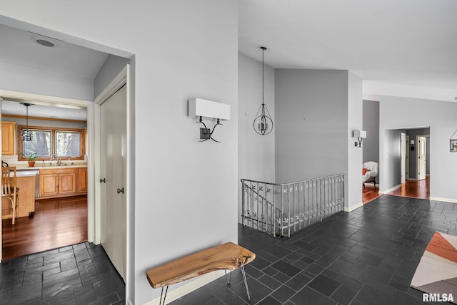 hall featuring baseboards, stone tile floors, a sink, and an upstairs landing