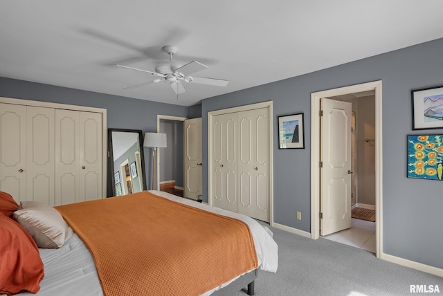 bedroom featuring multiple closets, light carpet, baseboards, ensuite bathroom, and ceiling fan