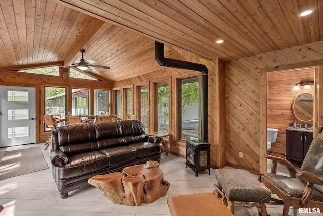 living room featuring a wood stove, wood ceiling, wooden walls, and a wealth of natural light
