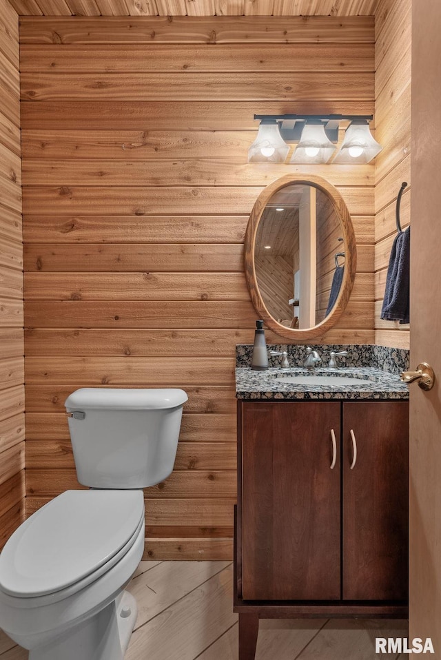 half bath with toilet, wood walls, and vanity