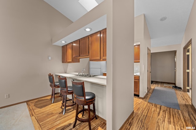 kitchen with baseboards, a kitchen bar, light countertops, brown cabinets, and a sink