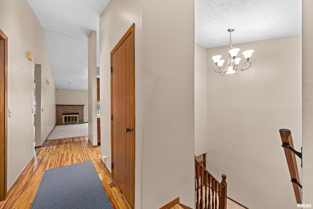 hall with a chandelier, a textured ceiling, an upstairs landing, and light wood finished floors
