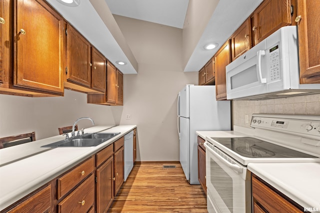 kitchen with white appliances, light wood-style floors, light countertops, tasteful backsplash, and a sink