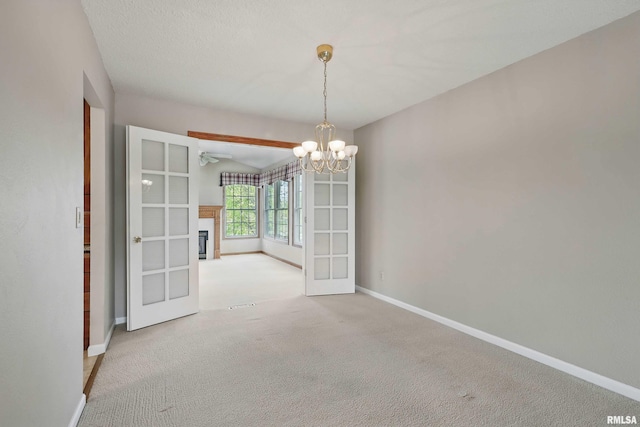 unfurnished dining area with an inviting chandelier, a glass covered fireplace, baseboards, french doors, and carpet