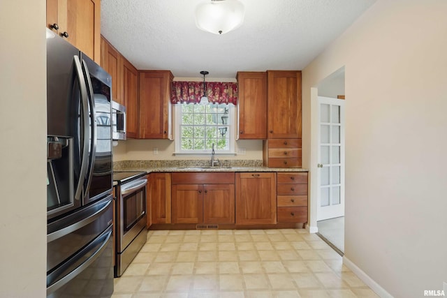kitchen with a sink, a textured ceiling, appliances with stainless steel finishes, and brown cabinets