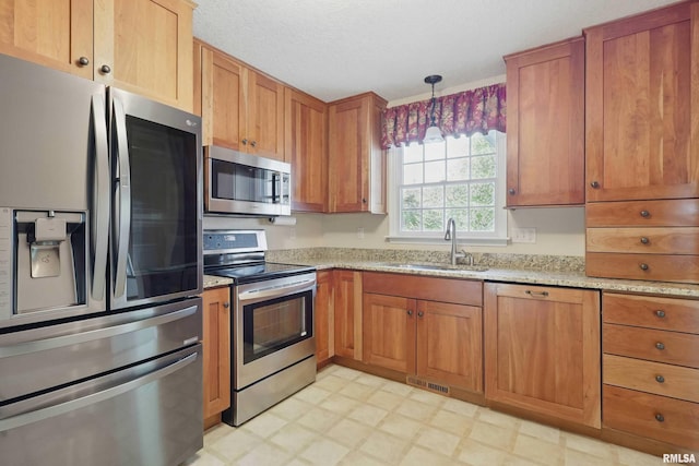 kitchen featuring visible vents, a sink, light stone counters, light floors, and stainless steel appliances