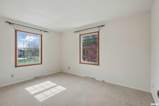 carpeted empty room with baseboards, a wealth of natural light, and visible vents