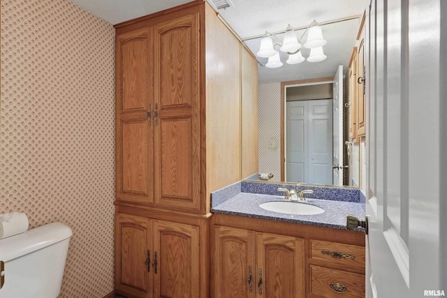 bathroom featuring vanity, toilet, and wallpapered walls
