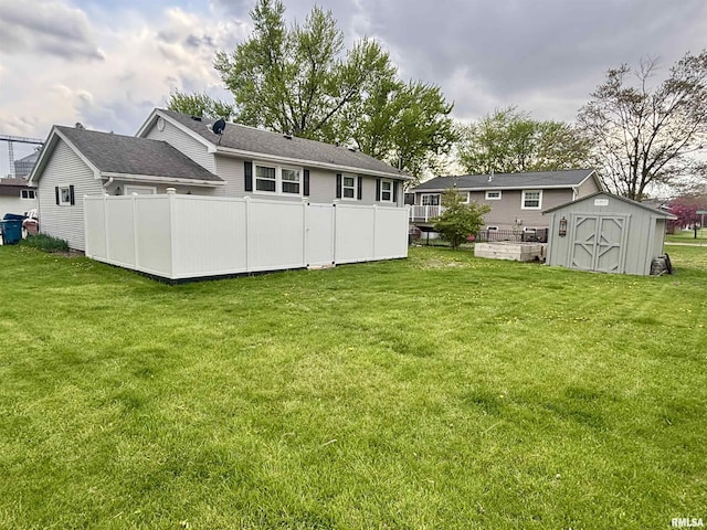rear view of house featuring a lawn, fence, an outdoor structure, and a storage unit