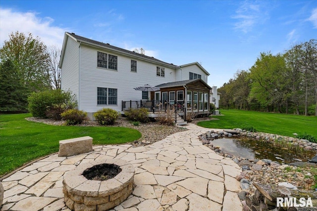 back of house with a garden pond, a sunroom, a patio area, a lawn, and a fire pit