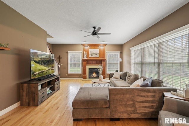 living area with a glass covered fireplace, baseboards, ceiling fan, and light wood-style flooring