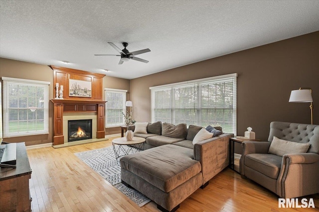 living room with a glass covered fireplace, a ceiling fan, light wood-type flooring, and a textured ceiling