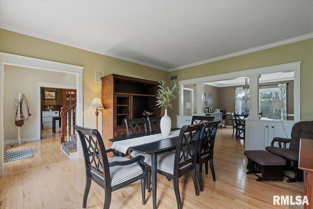 dining area with ornate columns, ornamental molding, light wood-style floors, and stairs
