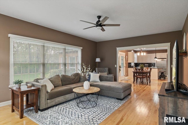 living area featuring baseboards, ceiling fan with notable chandelier, and light wood-style floors