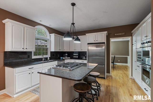kitchen with a sink, light wood-style flooring, stainless steel appliances, white cabinetry, and backsplash