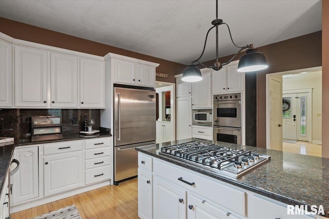 kitchen with light wood-type flooring, decorative backsplash, white cabinetry, and appliances with stainless steel finishes