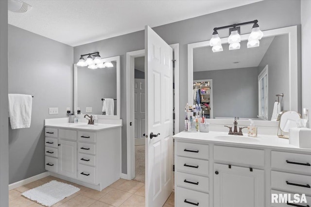 full bath featuring baseboards, two vanities, a sink, and tile patterned flooring
