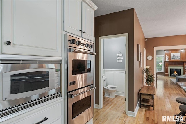 kitchen with a lit fireplace, white cabinets, open floor plan, stainless steel appliances, and light wood-style flooring