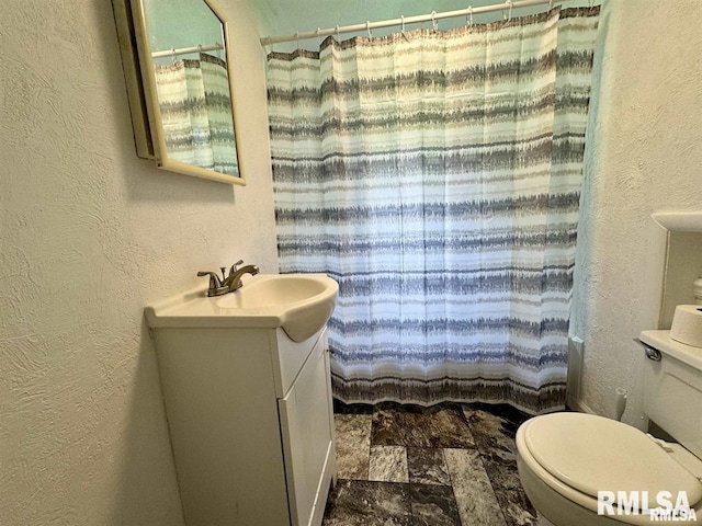 full bath featuring toilet, a textured wall, vanity, and a shower with shower curtain