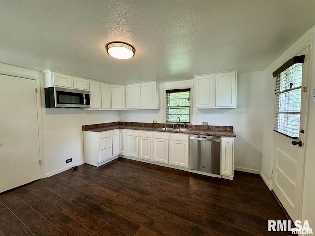 kitchen with appliances with stainless steel finishes, dark countertops, dark wood-style flooring, white cabinetry, and a textured ceiling