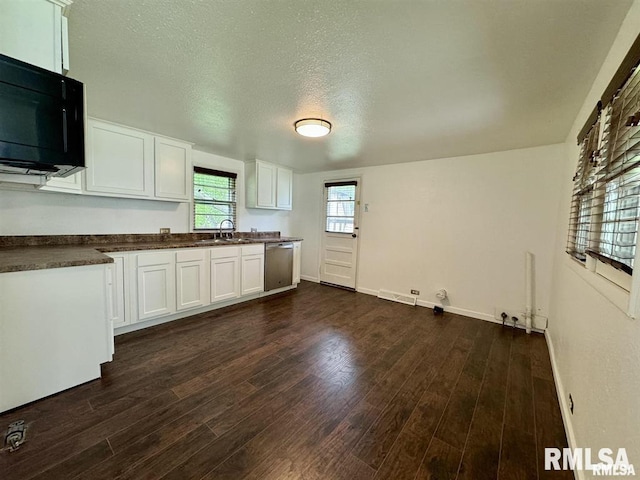 kitchen with black microwave, dark countertops, stainless steel dishwasher, a sink, and dark wood finished floors
