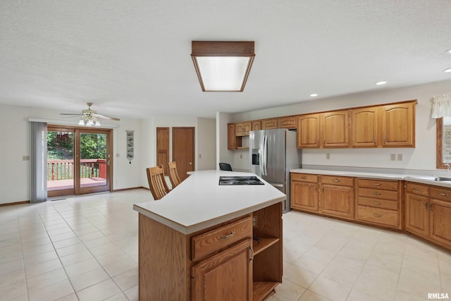 kitchen with ceiling fan, a kitchen island, black electric cooktop, light countertops, and stainless steel fridge with ice dispenser