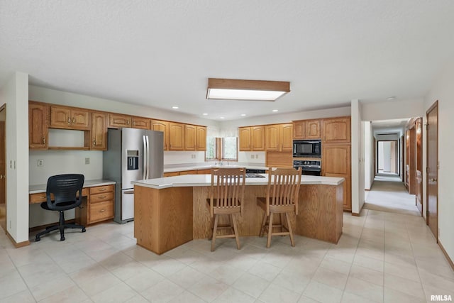 kitchen with a sink, built in study area, light countertops, a kitchen island, and black appliances