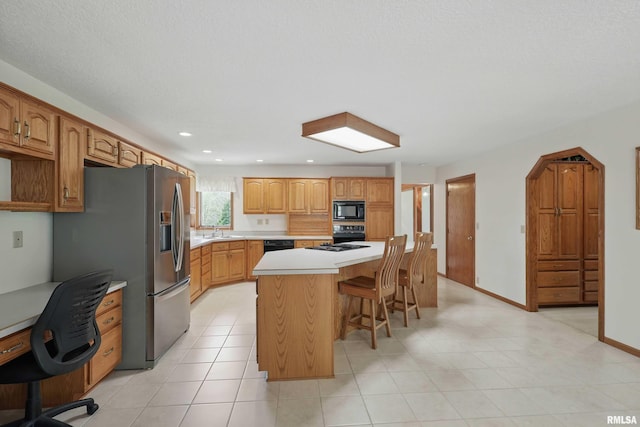 kitchen featuring a kitchen island, a kitchen breakfast bar, light countertops, a sink, and black appliances