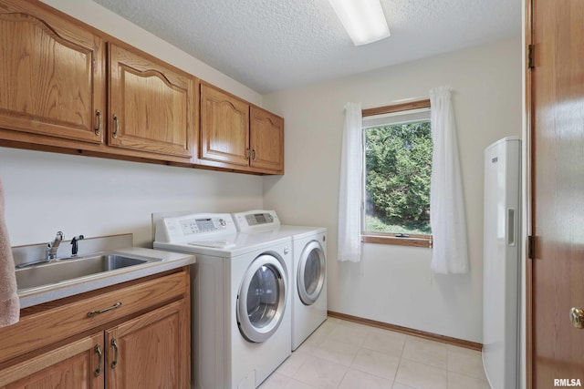 washroom with cabinet space, a sink, a textured ceiling, baseboards, and washing machine and dryer