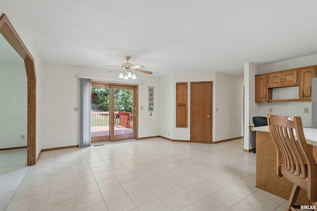 unfurnished living room with a textured ceiling, baseboards, a ceiling fan, and light tile patterned flooring