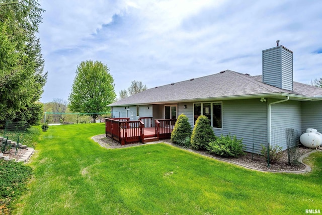 back of house with a yard, a wooden deck, roof with shingles, and a chimney