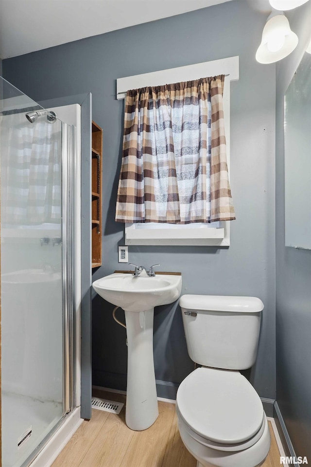bathroom with baseboards, a stall shower, toilet, and wood finished floors