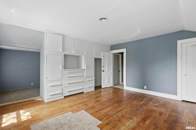 unfurnished bedroom featuring baseboards, wood-type flooring, vaulted ceiling, and visible vents